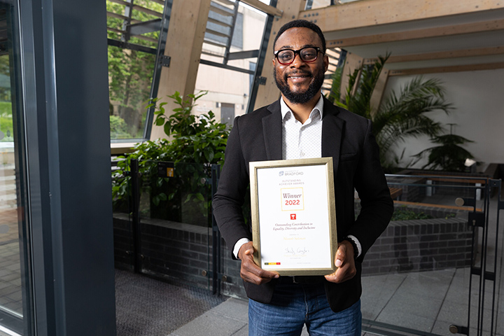 A smartly dressed student smiling at the camera holding a 'winners' certificate