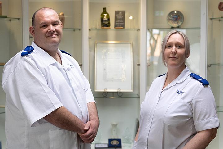 Two students in nursing uniform. They are both smiling at the camera