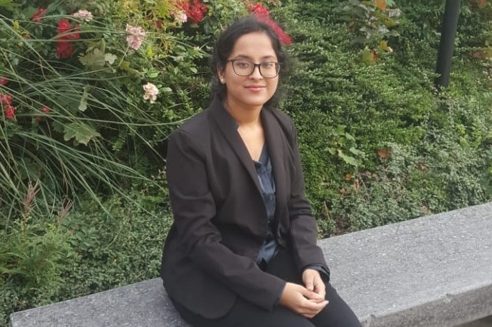 Sapna sat on a stone bench in front of some greenery.