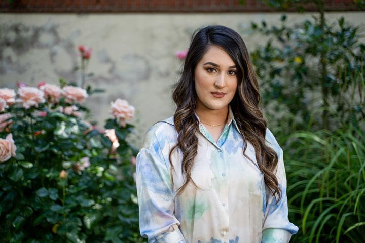 A person standing in front of some rose plants and a wall.