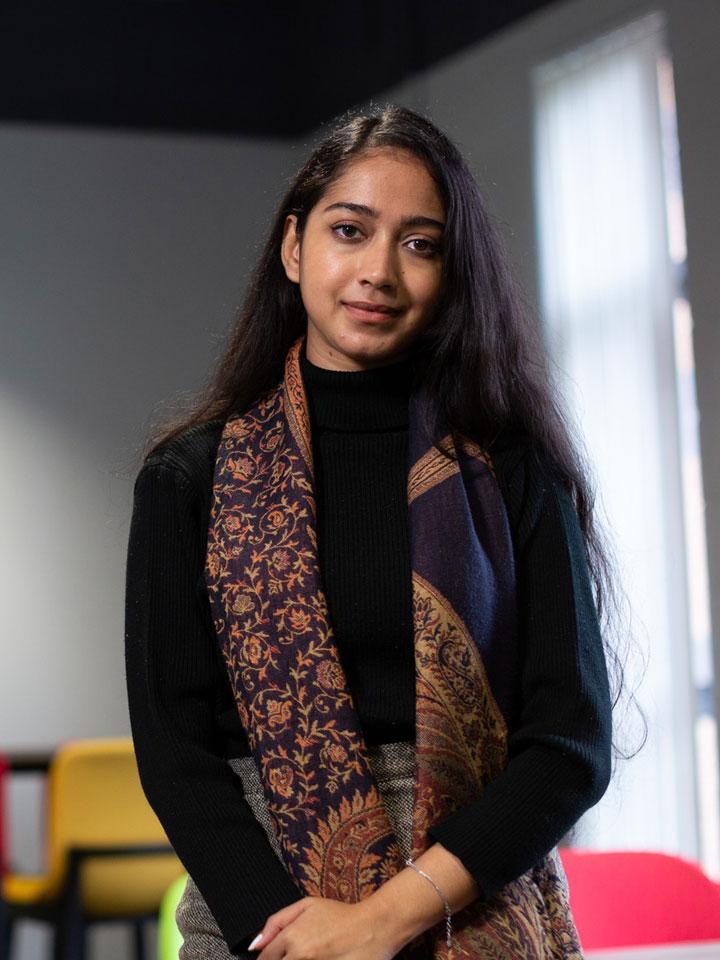 A person standing and facing the camera. There is some brightly coloured furniture in the background.