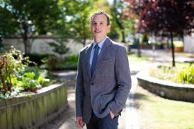 A person wearing a suit, standing outside on a path in a garden.