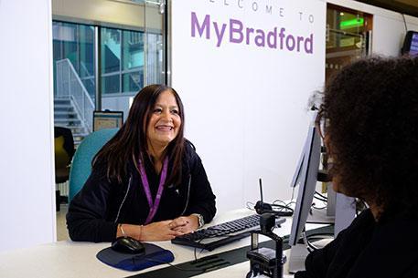 A MyBradford advisor sitting at a desk facing a student and chatting.