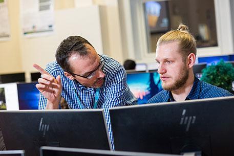 A lecturer and student having a discussion sitting in front of two computer monitors.