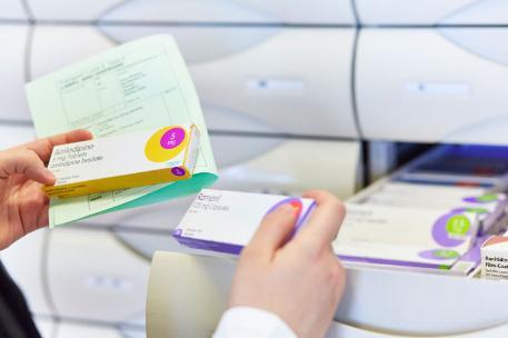 A pharmacy student's hand selecting medicines from a drawer