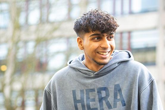 A student sitting on a wall smiling with a block of flats in the background.