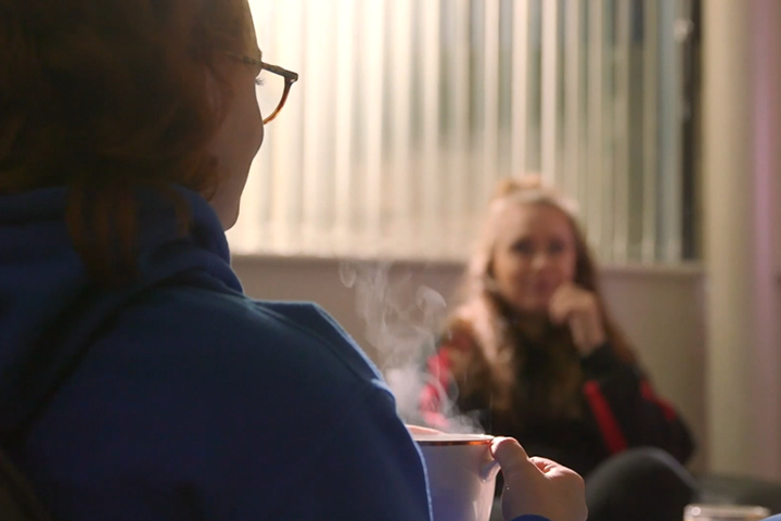 Amy sitting with a cup of tea and talking to a friend.