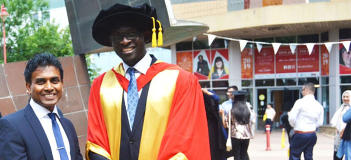 A person wearing a yellow and red graduation gown standing next to another person wearing a blue suit.