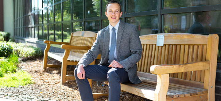 A person wearing a suit, sitting on a bench in the University of Bradford Peace Garden.