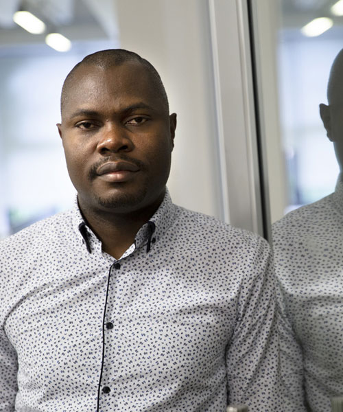 Student Olushola facing the camera and leaning with his shoulder on a mirror. His reflection is visible in the mirror.