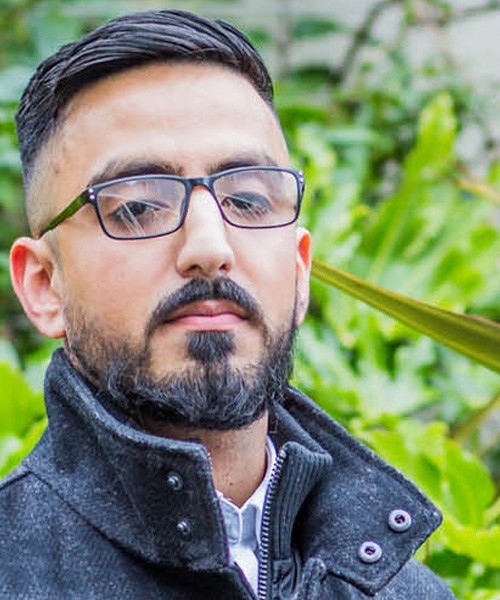 Student looking intensely towards the camera while standing in front of green leaves