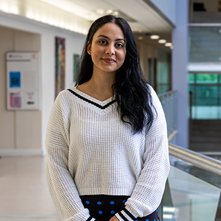 A student wearing a white cable-knitted jumper smiles at the camera