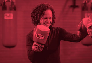 Woman wearing boxing gloves smiling with an outstretched arm. 